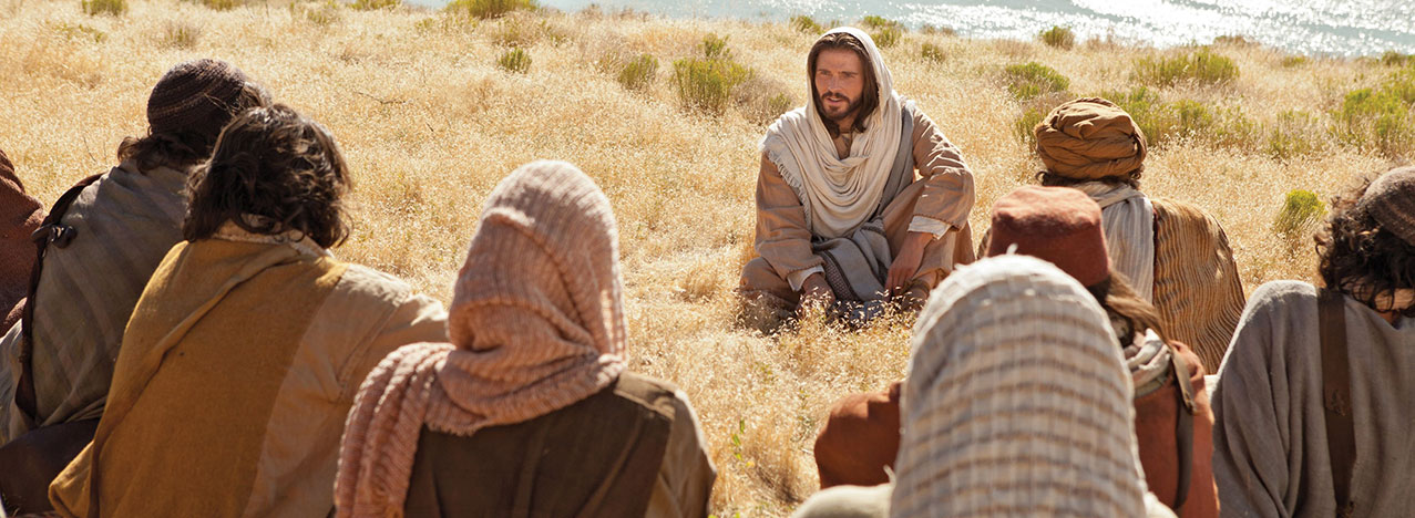 Jesus Christ teaching a group of people in a field by the sea